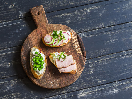 Sandwiches with feta, green peas, radish, cucumber and smoked meat on wooden rustic board. Delicious breakfast or snackの写真素材