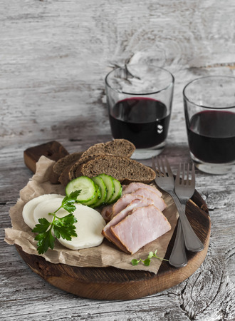 Smoked pork, cheese and two glasses of red wine on a light rustic wood background. Delicious foodの写真素材
