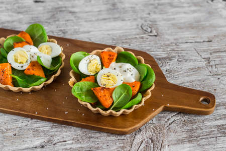 Fresh salad with roasted pumpkin, spinach and quail eggs served in tartlets from whole wheat flour.の写真素材