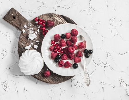 Raspberries, red and black currants, a meringue on a rustic cutting board, on bright backgroundの写真素材