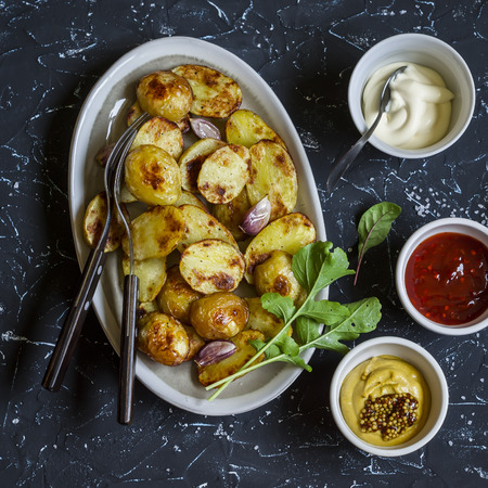 Baked potatoes and sauce him - homemade mayonnaise, ketchup and mustard. Delicious lunch or snack. On dark stone backgroundの写真素材