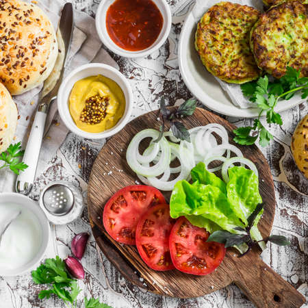 Ingredients for cooking vegetarian burgers - zucchini burgers, homemade buns, tomatoes, onions, herbs, spices and sauces on a light stone background. The view from the topの写真素材