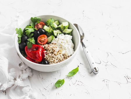 Mediterranean quinoa bowl with avocado, cucumbers, olives, tomatoes, feta cheese, arugula. On a white background. Delicious healthy vegetarian foodの写真素材