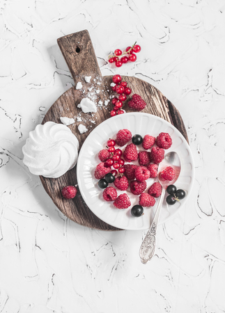 Raspberries, red and black currants, a meringue on a rustic cutting board, on bright backgroundの写真素材