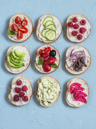 Variety of sandwiches - sandwiches with cheese, tomatoes, anchovies, roasted peppers, raspberries, avocado, bean pate, cucumber, olives. On a blue background, top view.の写真素材
