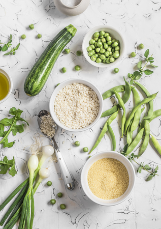 Raw ingredients - rice, cous cous, zucchini, green beans and peas, olive oil on a light background. Healthy vegetarian foodの写真素材