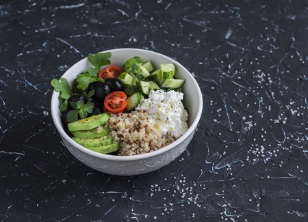 Mediterranean quinoa bowl with avocado, cucumbers, olives, tomatoes, feta cheese, arugula. On a dark background. Delicious healthy vegetarian foodの写真素材