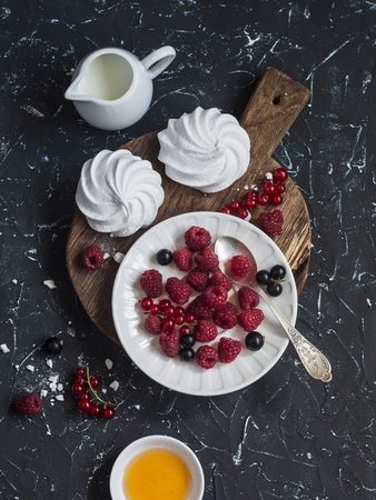 Raspberries, red and blackcurrants, a meringue, cream on a rustic cutting board, on dark backgroundの写真素材