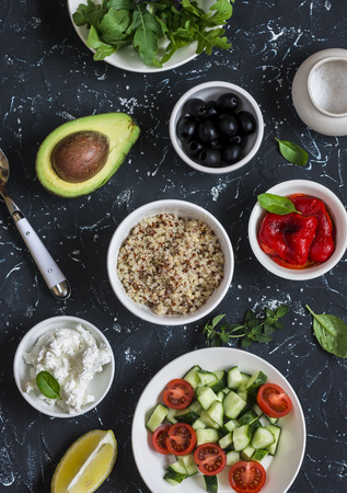 Quinoa, avocado, roasted peppers, fresh cucumbers and tomatoes, arugula, goat cheese - ingredients for salad. On a dark background, top viewの写真素材