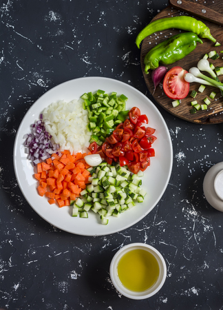 Fresh chopped vegetables - tomatoes, zucchini, carrots, tomatoes, onions, peppers on a dark background. Ingredients for ratatouille. Top viewの写真素材