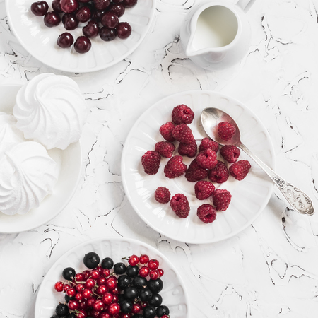 Raspberries, red and black currants, cherry, a meringue, cream on light backgroundの写真素材