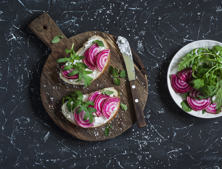 Sandwiches with feta cheese, radishes, arugula on rustic cutting board on a dark background. Healthy breakfast or snackの写真素材
