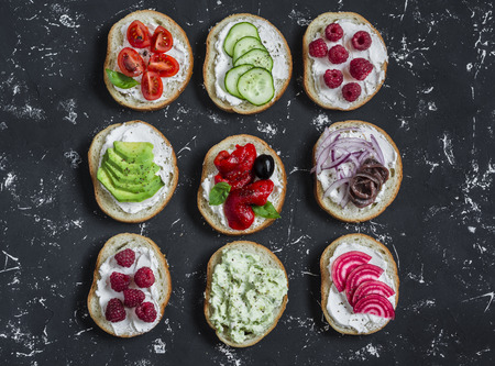 Variety of sandwiches - sandwiches with cheese, tomatoes, anchovies, roasted peppers, raspberries, avocado, bean pate, cucumber, olives. On a blue background, top view.の写真素材