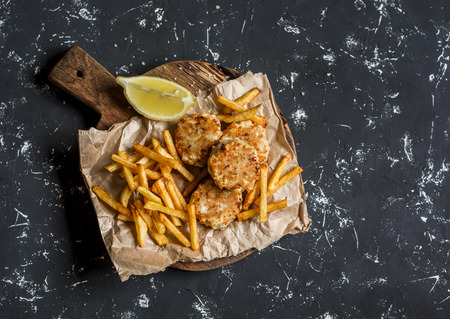 Fish meatballs and potato chips on rustic cutting board on a dark background. Top viewの写真素材