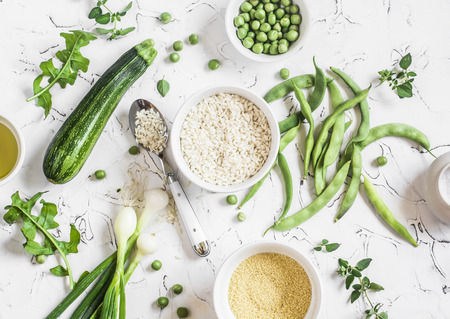 Raw ingredients - rice, cous cous, zucchini, green beans and peas, olive oil on a light background. Healthy vegetarian foodの写真素材