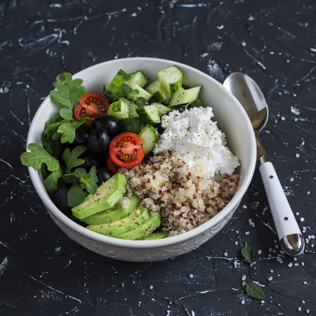Mediterranean quinoa bowl with avocado, cucumbers, olives, tomatoes, feta cheese, arugula. On a dark background. Delicious healthy vegetarian foodの写真素材