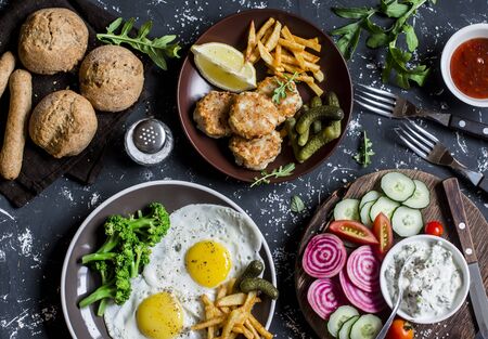 Lunch table - fried eggs, fish balls, potato chips, vegetables, sauces, homemade bread on a dark background. Rustic style, top viewの写真素材