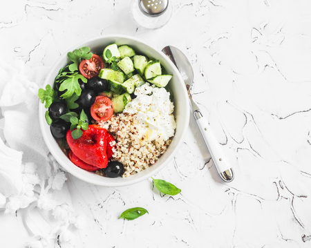 Mediterranean quinoa bowl with avocado, cucumbers, olives, roasted pepper, feta cheese, arugula. On a white background. Delicious healthy vegetarian foodの写真素材