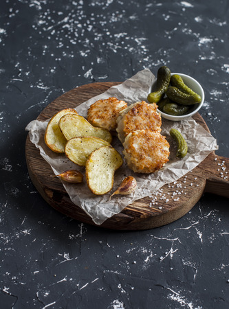 Fish balls and baked potatoes on wooden cutting board on dark backgroundの写真素材