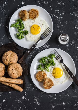 Fried eggs, broccoli, chicken meatballs, homemade whole wheat bread - tasty simple dinner. On a dark background, top viewの写真素材