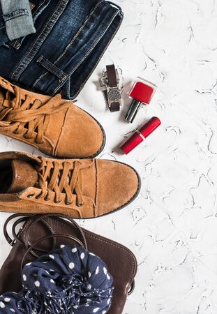 Women's clothing and accessories - suede boots, jeans, leather bag, scarf, red nail polish and lipstick. On a light background, top viewの写真素材