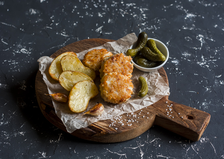 Fish balls and baked potatoes on wooden cutting board on dark backgroundの写真素材