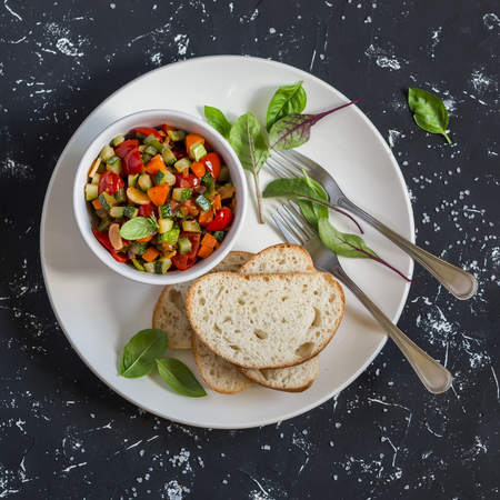 Quick ratatouille and bread on a white plate on a dark background. Delicious healthy vegetarian food. Top viewの写真素材