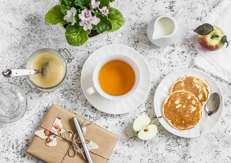 Tea, pancake, apple sauce, homemade gift in kraft paper, flower violet on a light background. Romantic breakfast table. Vintage style, top viewの写真素材
