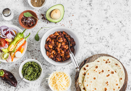 Lunch or snack - tortilla, stewed beans, vegetables, cheese, spicy green chile sauce. Delicious, vegetarian food. On a light background, top viewの写真素材