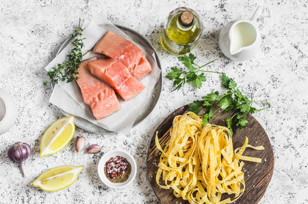 Ingredients for cooking lunch - raw salmon, dry pasta tagliatelle, cream, olive oil, spices and herbs. On a light background, top viewの写真素材