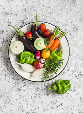 Fresh vegetables - eggplant, radish, bell pepper, tomatoes, thyme, oregano in an enamel bowl on a light background. Top viewの写真素材