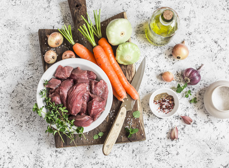 Ingredients for cooking dinner - raw beef meat, carrots, squashes, onions, garlic, thyme, spices, olive oil. On a light background, top viewの写真素材