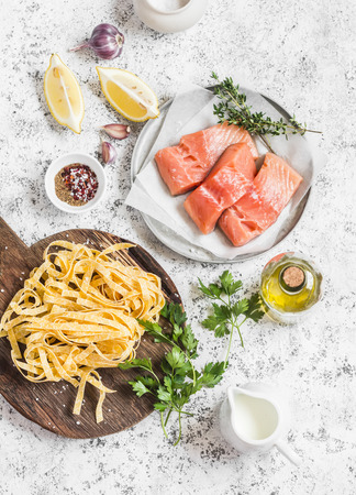 Ingredients for cooking lunch - raw salmon, dry pasta tagliatelle, cream, olive oil, spices and herbs. On a light background, top viewの写真素材