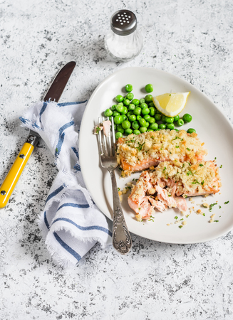Crumbed baked salmon and green peas on a white plate on a light background. Healthy foodの写真素材