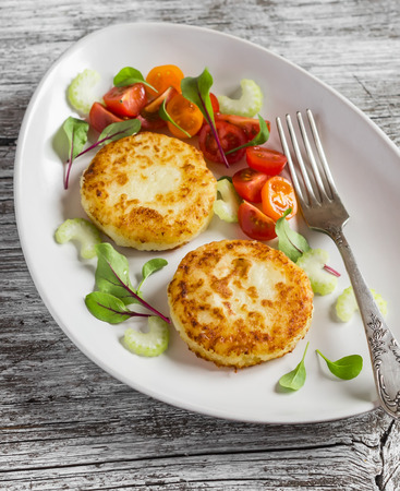 Potato patties and fresh tomato and celery salad on a light ceramic plate on  wooden background.の写真素材