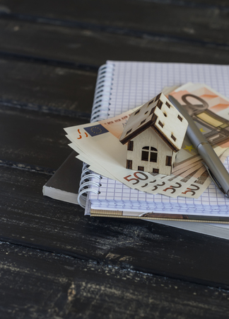 Model house, Euro banknotes, notepad on dark wooden background. The concept of buying, selling, trading, housing construction.の写真素材