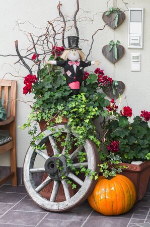 Halloween decoration - pumpkin, Scarecrow, old wooden wheel near the door of the houseの写真素材