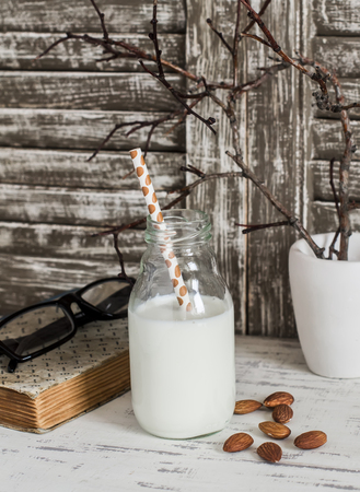 Almond milk and almonds, a book, glasses on rustic light wood table. Still life in vintage styleの写真素材