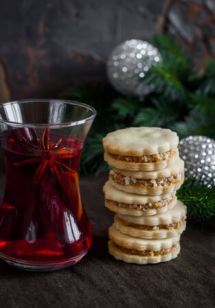 Tea with spices and herbs and shortbread biscuits with caramel cream and walnuts on a dark surfaceの写真素材