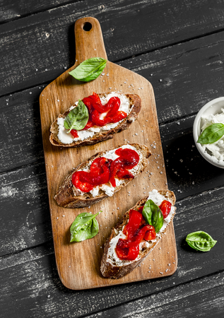 Open sandwich cheese, roasted red sweet peppers and basil on a dark wooden boardの写真素材
