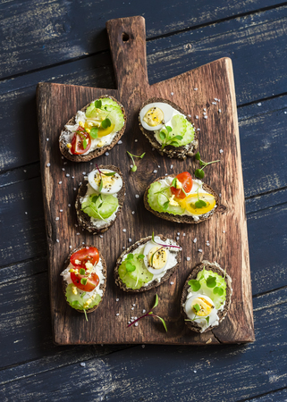 Sandwiches with soft cheese, quail eggs, cherry tomatoes and celery. Delicious healthy snack or Breakfast. On a wooden rustic boardの写真素材
