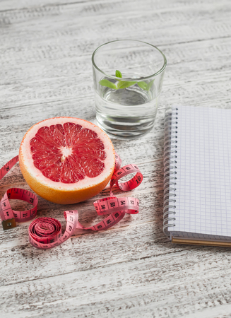 Open a blank Notepad, a grapefruit, a glass of water and measuring tape on a light wooden table. The concept of a healthy lifestyle, healthy food, dietの写真素材