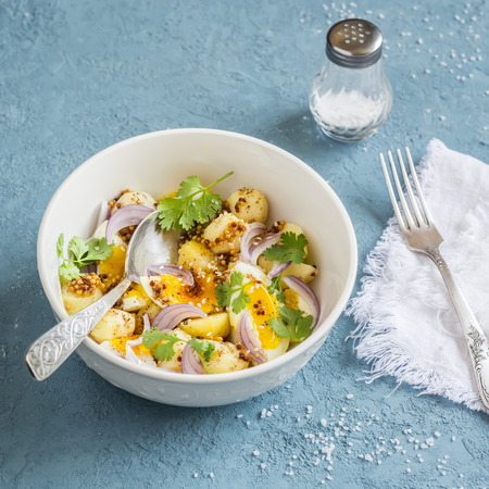 Potatoes and boiled egg salad with olive oil and mustard dressing. On a blue background, top viewの写真素材