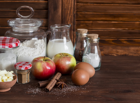 Ingredients and tools for baking - flour, eggs, butter, apples, cinnamon on a brown rustic wooden surface.  Ingredients for baking apple pieの写真素材
