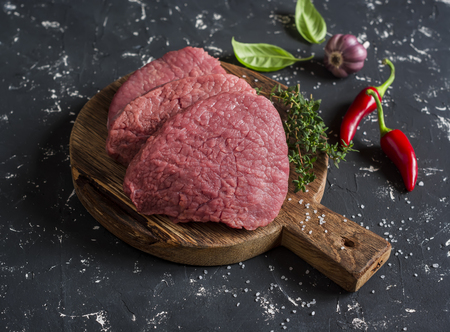Raw beef chops on a wooden cutting board on a dark backgroundの写真素材
