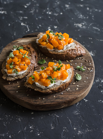 Pumpkin and goat's cheese bruschetta on a wooden cutting board on dark background. Healthy vegetarian snackの写真素材