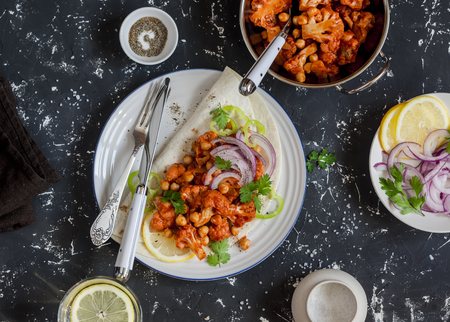 Spicy cauliflower in tomato sauce with chickpeas on flatbread. Tasty vegetarian food. On a dark background, top viewの写真素材
