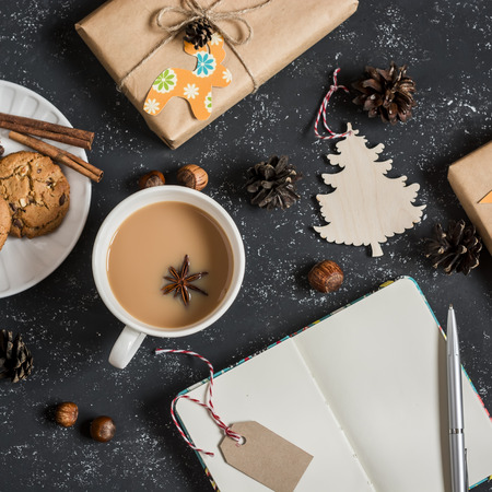 Christmas background - homemade gifts in craft paper, christmas ornaments, note book, tea and biscuits. On a dark background, top viewの写真素材