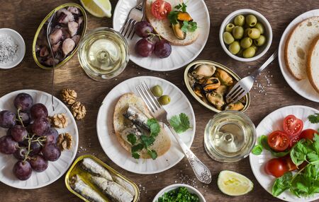 Seafood snacks table - canned sardines, mussels, octopus, grape, olives, tomato and two glasses white wine on wooden table, top view. Flat layの写真素材