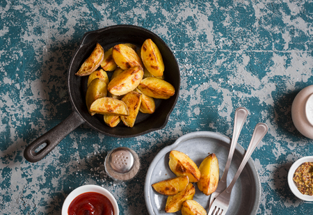 Baked potatoes in a cast iron frying pan on wooden background, top viewの写真素材